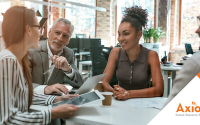 Group of diverse professionals engaged in a collaborative meeting at a modern office, discussing HR strategies and solutions, featuring Axiom Human Resource Solutions branding in the corner.
