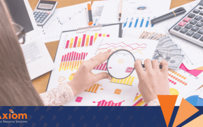 Hands analyzing colorful graphs and charts with a magnifying glass on a desk filled with financial documents and a calculator, featuring Axiom Human Resource Solutions branding.