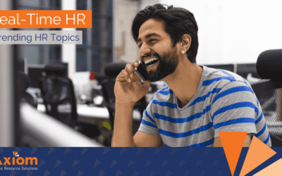 Smiling man on a phone call in an office setting, representing real-time HR discussions and trending HR topics for Axiom Human Resource Solutions.