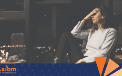 Woman sitting in an office, looking stressed and contemplative, representing trauma in the workplace, with Axiom Human Resource Solutions logo in the foreground.