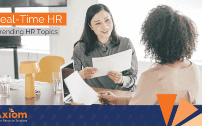 Two women engaged in a discussion about HR topics, holding documents, in a modern office setting, featuring Axiom Human Resource Solutions branding.