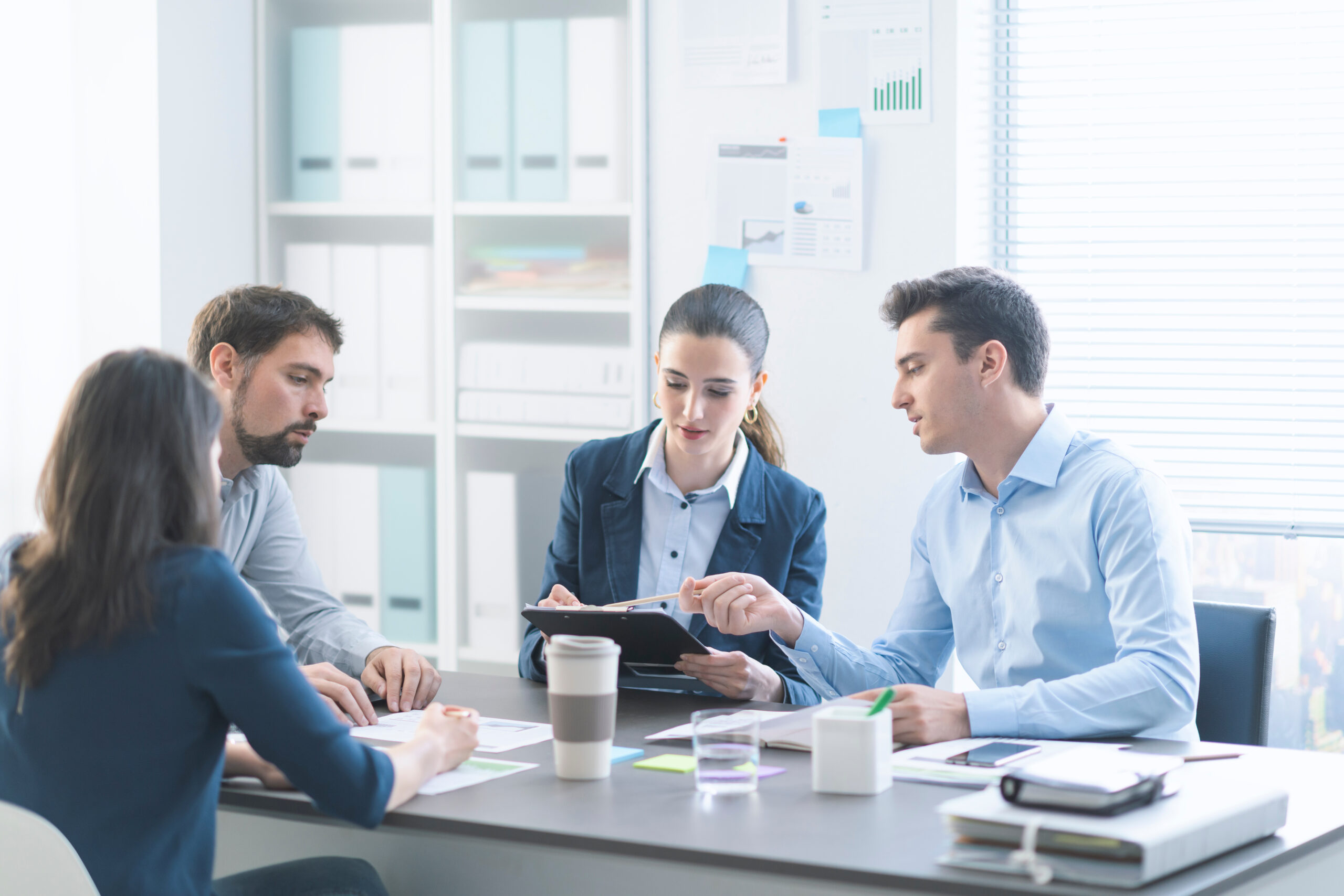 Group of professionals discussing HR strategies around a table, with documents and a coffee cup, highlighting collaboration in addressing human resource issues.