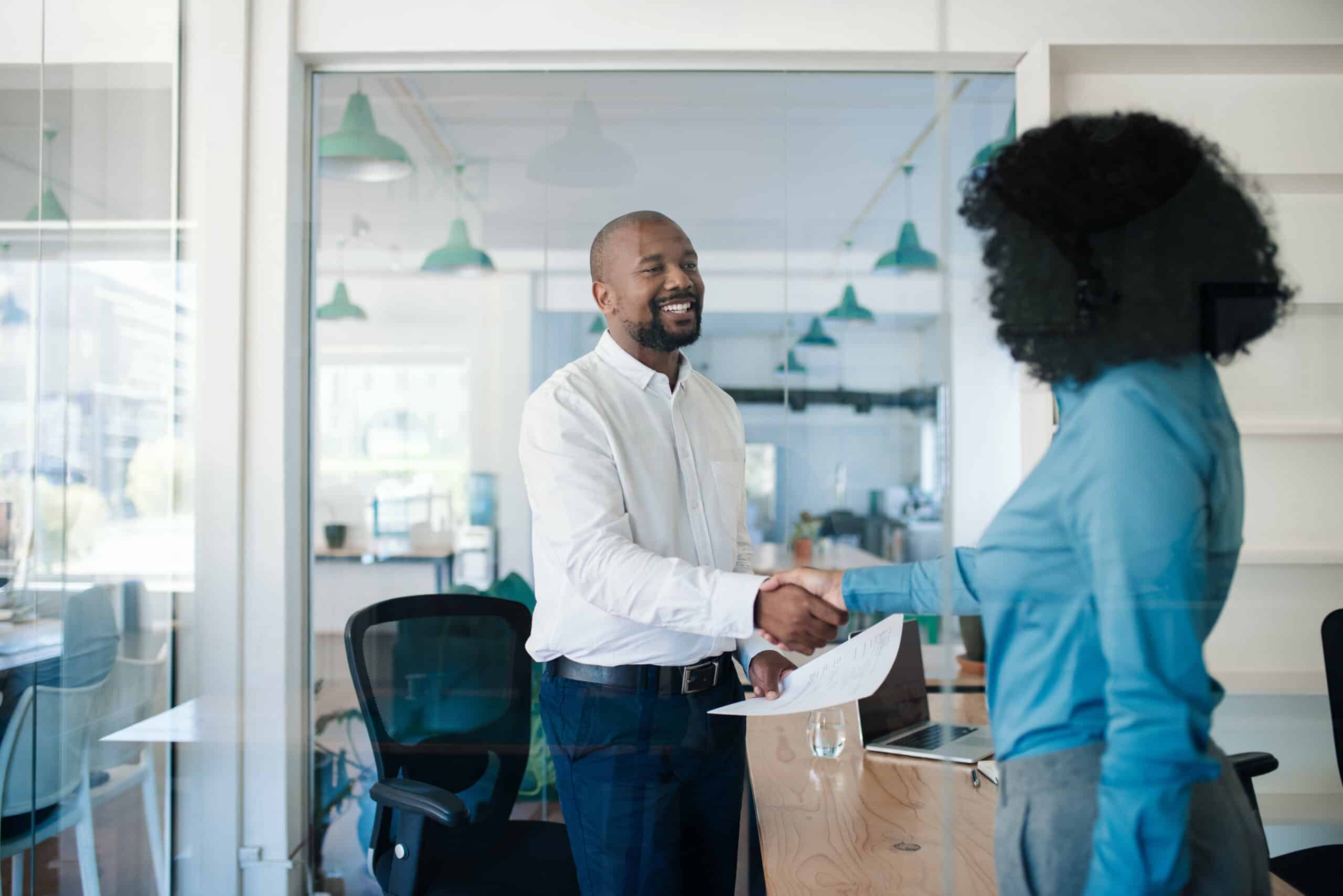 Business professionals shaking hands in a modern office setting, emphasizing collaboration and employee engagement in the context of updated employee handbooks for 2025.