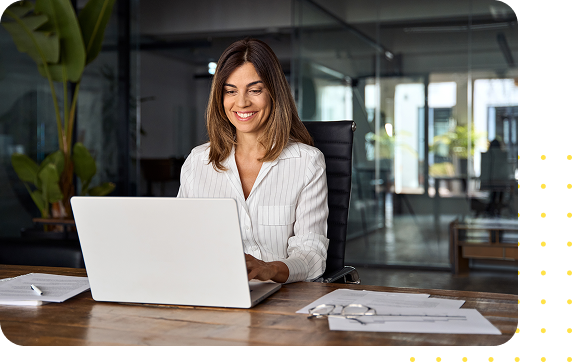 All-in-One HR Solutions That Fit Your Industry Smiling woman in a striped blazer working on a laptop in a modern office, representing Axiom HRS's tailored HR solutions for various industries.