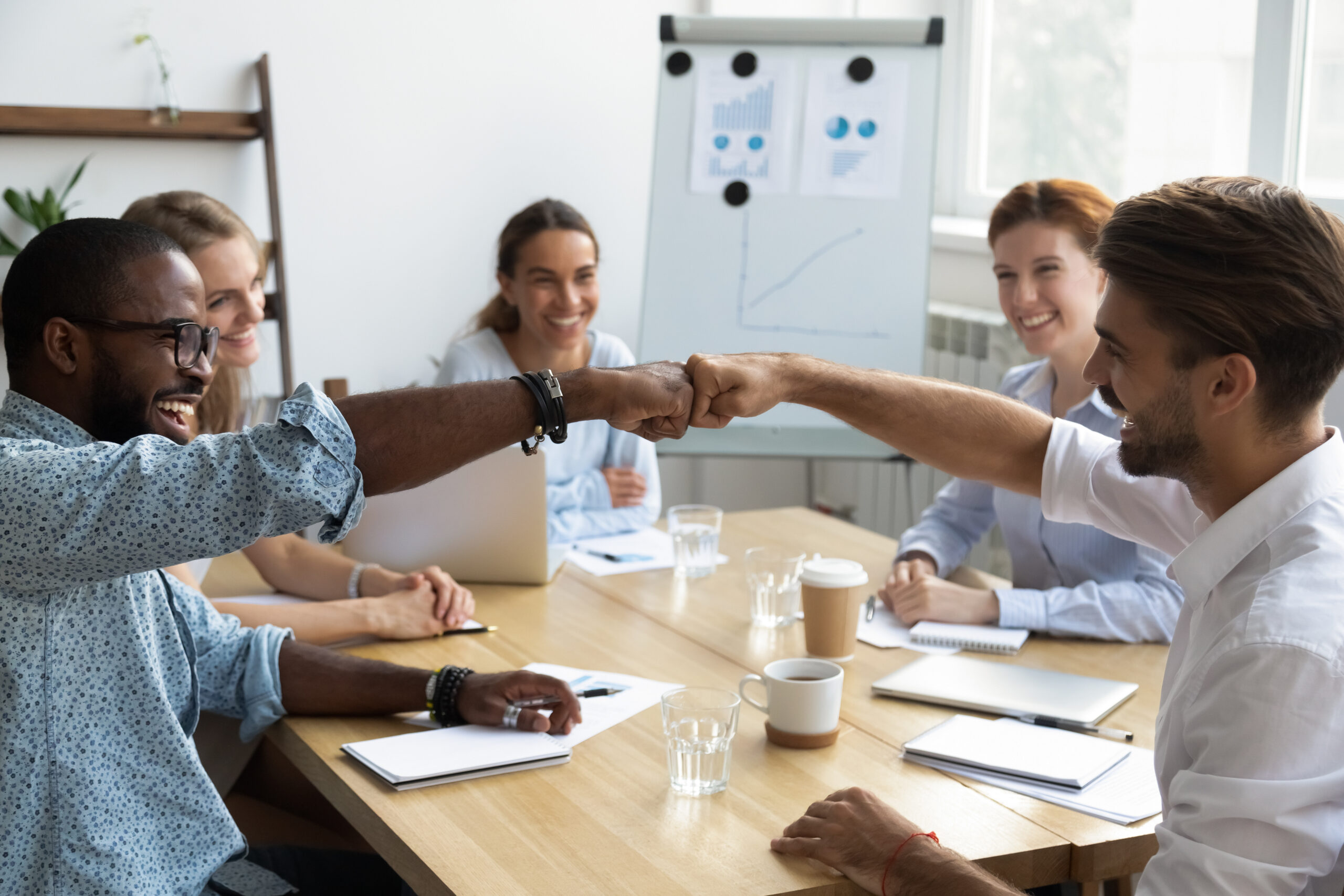 Group of diverse colleagues engaging in a positive interaction during a meeting, emphasizing teamwork and collaboration, with charts and graphs on a whiteboard in the background, reflecting a data-driven approach to workplace culture.